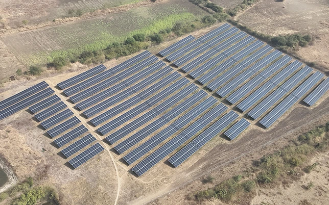 Ground Mount Solar Survey 3 Aerial drone view of a large ground-mounted solar panel farm surrounded by dry terrain and green fields in India