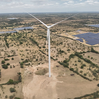 Drone aerial view of a wind turbine alongside large-scale solar panel arrays at a hybrid renewable energy site in India