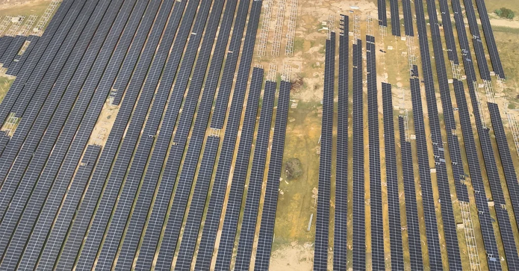 Aerial view of a large utility-scale ground-mounted solar energy plant in India showing rows of PV panels across an expansive site
