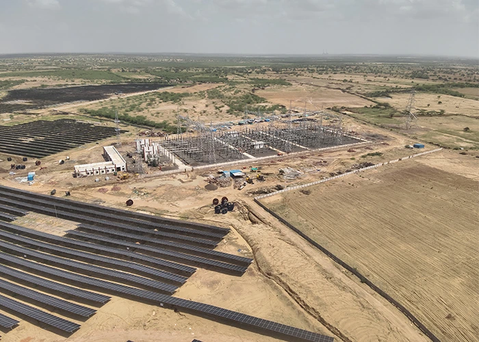 Wide-angle drone view of a large utility-scale solar park in India showing installed module rows, active grid substation construction, transmission towers, and the sheer site scale impossible to monitor on foot.