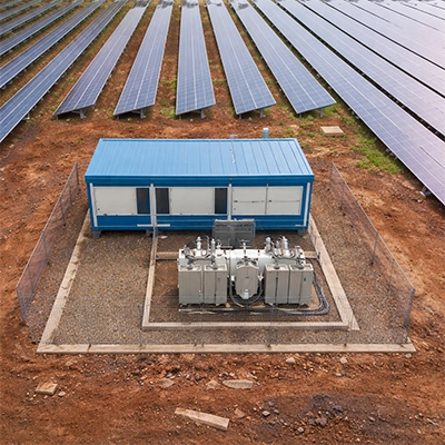 Drone view of a completed solar transformer station with blue containerised control cabin and dual transformer units installed between active module rows — documenting civil and electrical completion status for weekly progress reporting.