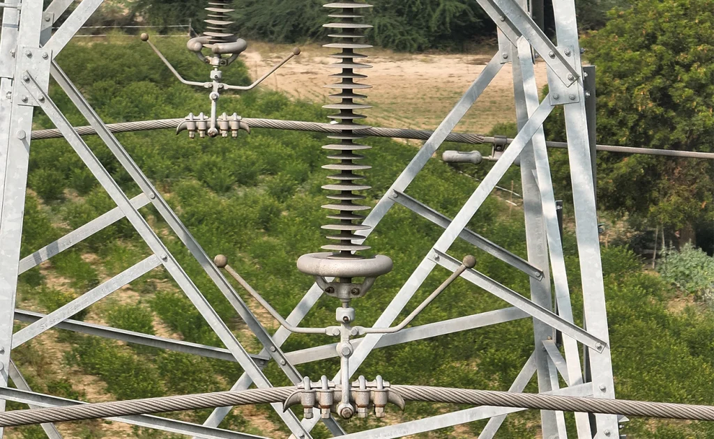 Close-up drone photograph of disc insulator string, arcing horns, and conductor clamp hardware on a high-voltage transmission tower, used for defect detection during drone-based transmission line inspection in India.