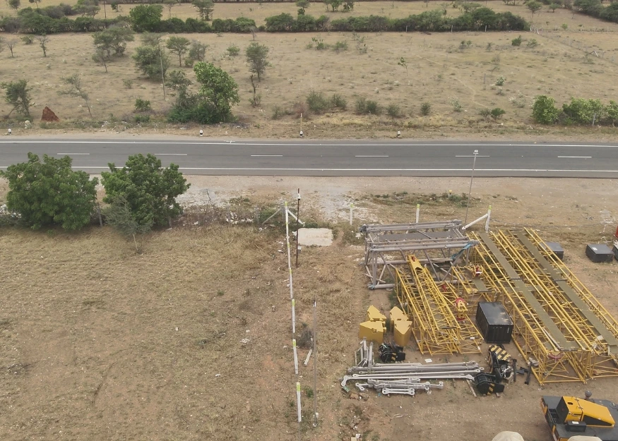 Drone shot of wind farm construction site showing tower components, crane parts, and equipment laydown area near access road in India