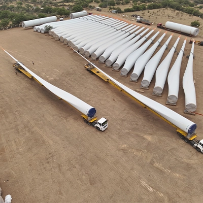 Aerial drone view of wind turbine blades staged on heavy transport vehicles at a wind farm logistics yard in India
