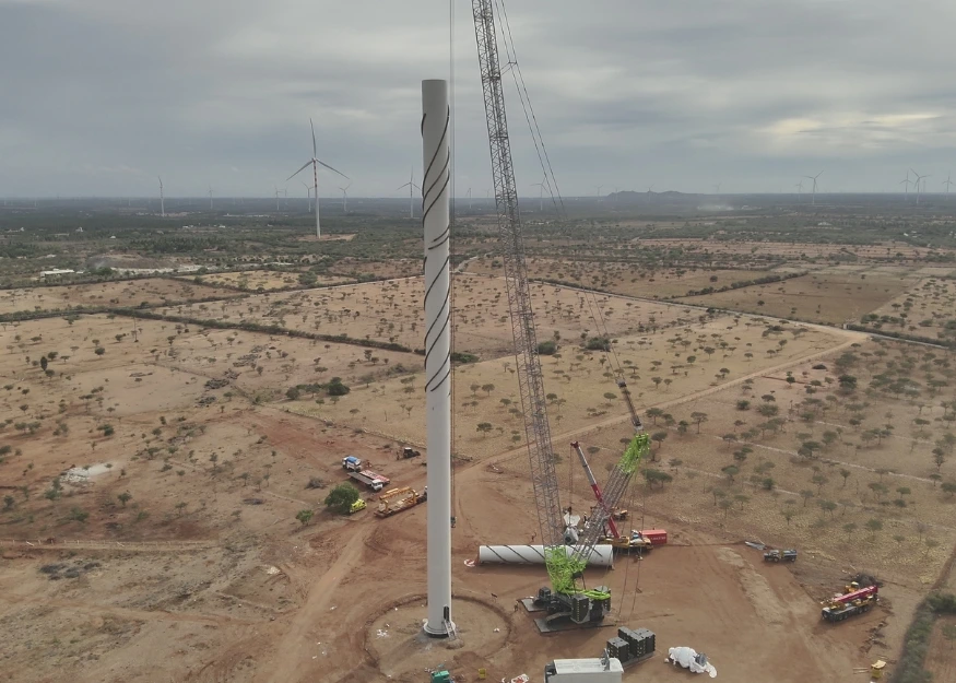 Drone view of wind turbine tower erection with cranes, construction vehicles, and multiple turbines visible across a wind farm site in India.