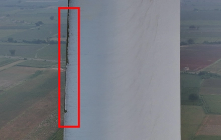Aerial drone image of wind turbine blade showing paint peeling along leading edge, red rectangle highlighting defect zone during UAV inspection in India