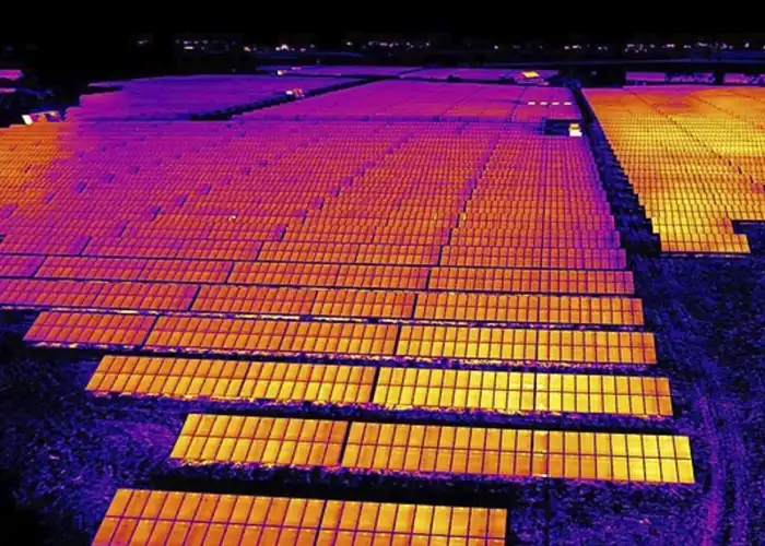Aerial thermal image of utility-scale solar farm showing orange-yellow panel surfaces against purple-violet cooler ground