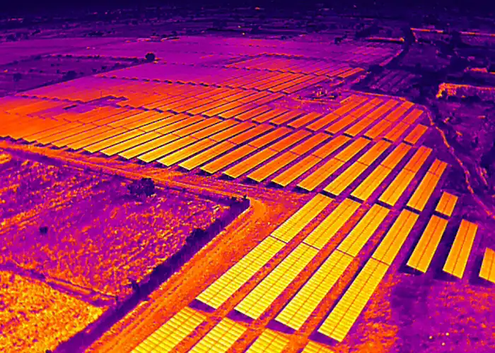 Aerial radiometric thermal image of utility-scale solar farm showing panel arrays in yellow-orange across purple background