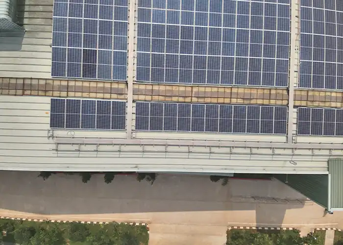 Aerial photo of rooftop solar panel rows along a building edge with maintenance walkway and ground visible below