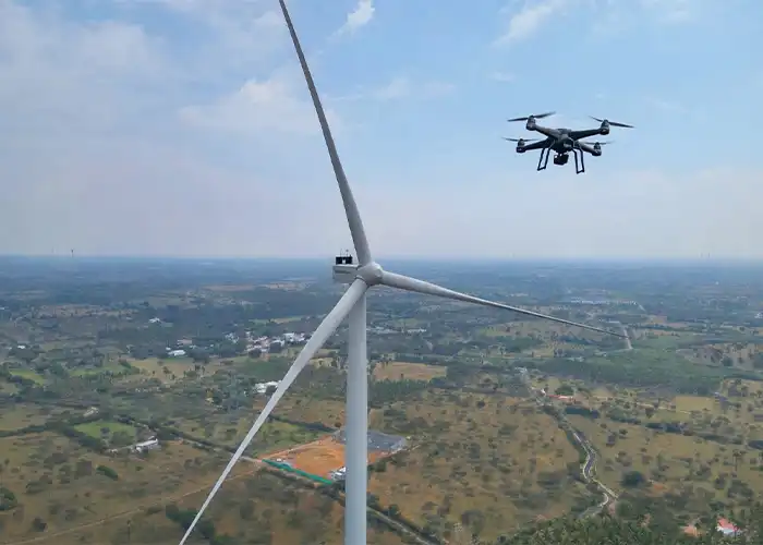 Quadcopter drone with camera hovering at nacelle height close to wind turbine blade during aerial inspection, India