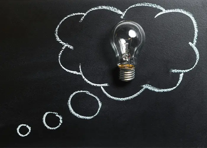 Incandescent light bulb inside chalk-drawn thought bubble on blackboard representing innovation concept