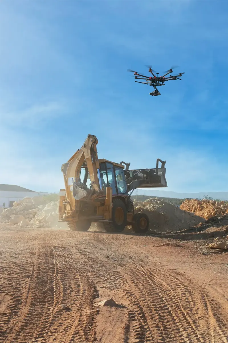 Octocopter drone with camera gimbal monitoring backhoe loader during active excavation in open-cast mining site