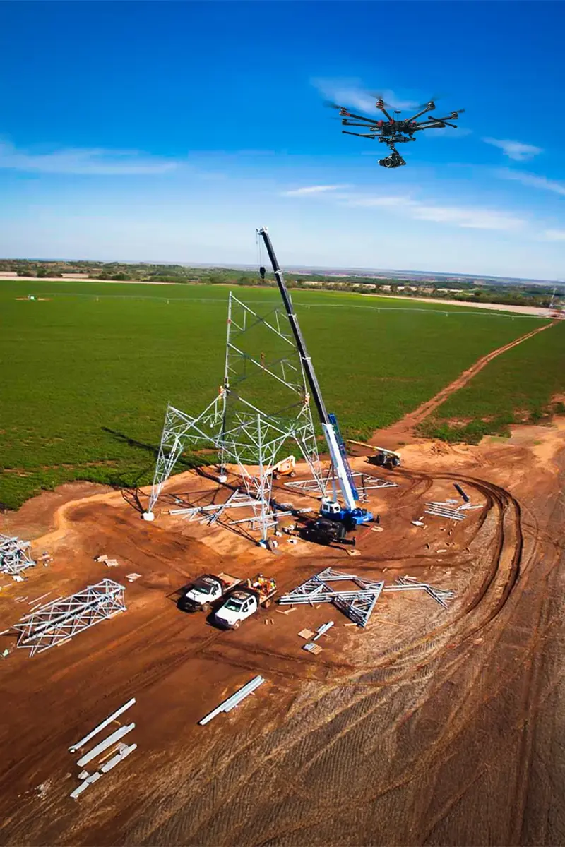 Octocopter drone monitoring mobile crane erecting lattice steel transmission tower at rural construction site