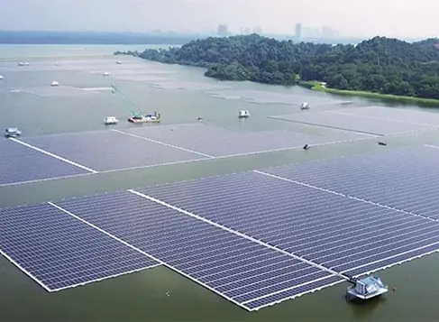 Aerial view of large floating solar farm with rectangular panel arrays on water body and forested island background