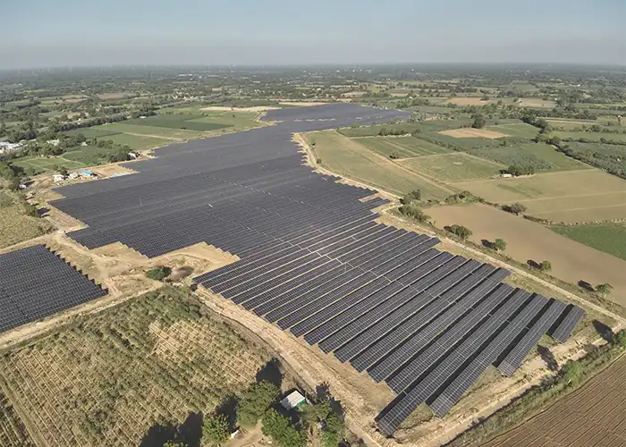 Aerial view of large ground mount solar farm surrounded by agricultural fields and tree plantations in Indian rural landscape