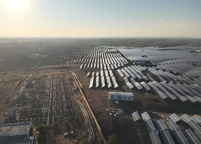 Aerial view of ground mount solar farm showing panel arrays, electrical substation infrastructure, control building, and access road on dry terrain