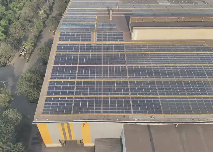 Aerial view of industrial warehouse rooftop densely covered with solar panels in organised rows, yellow building facade visible below