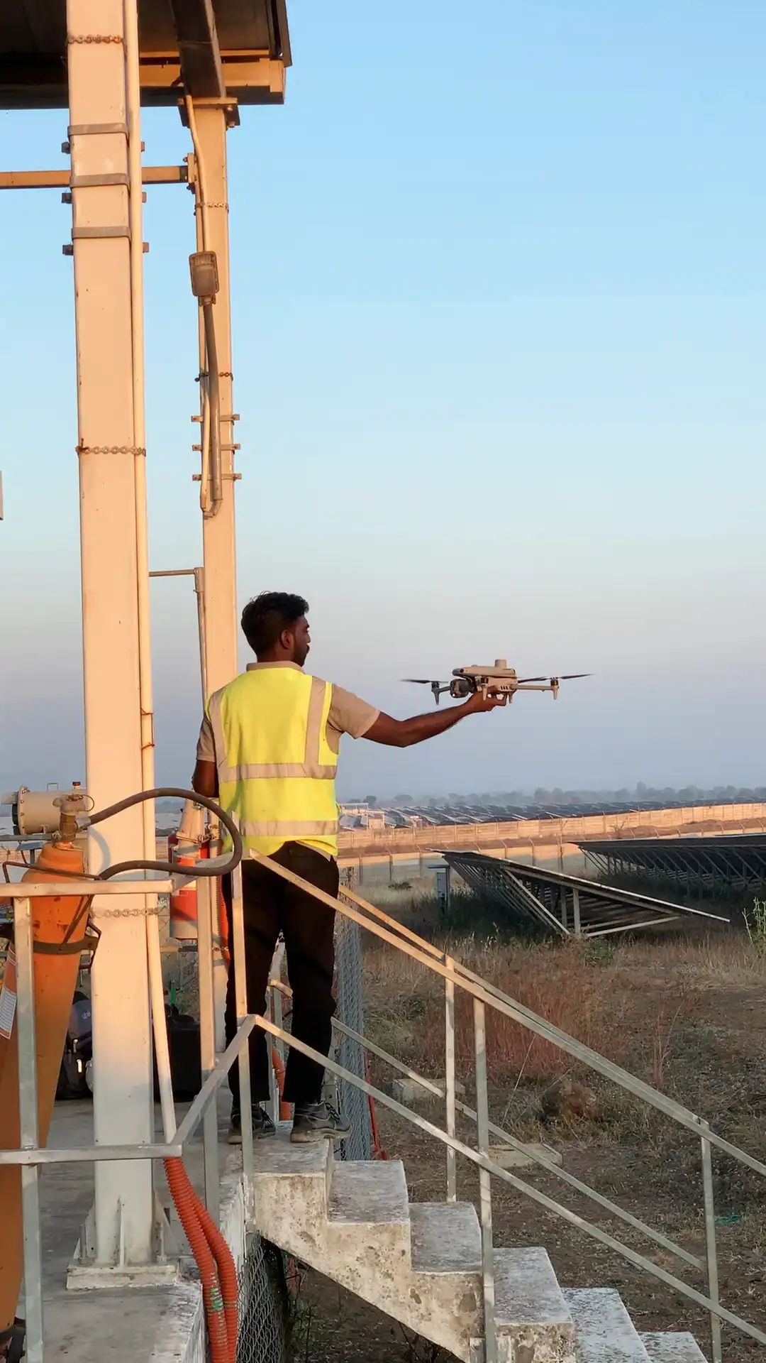 Lesoko pilot in hi-vis vest hand-launching drone at ground-mounted solar farm during early morning inspection