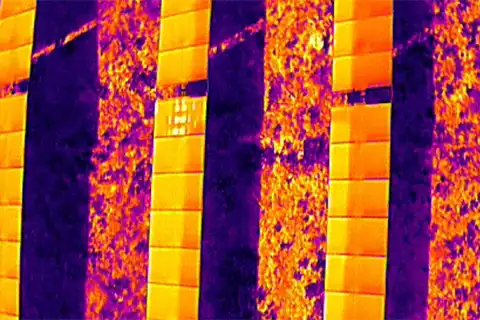 Aerial thermal image showing multiple distributed hotspot anomalies across solar panel strings