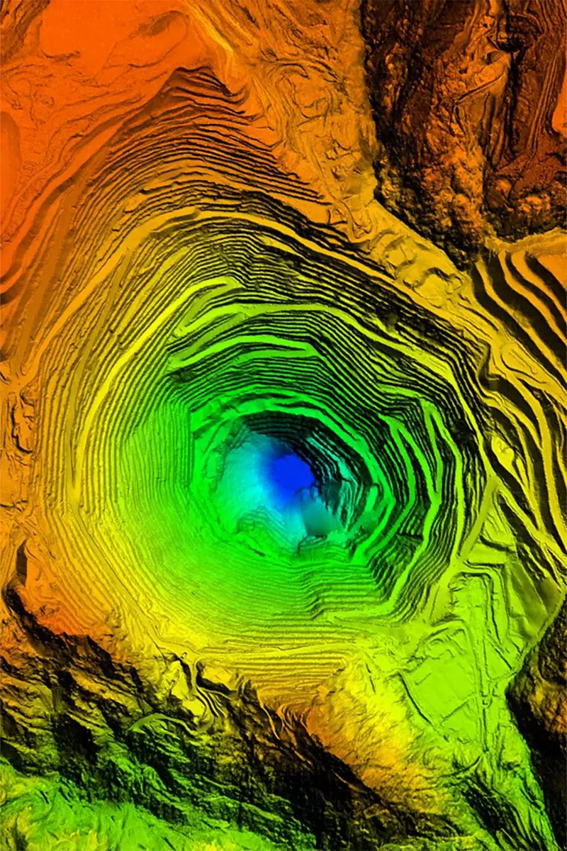 Colour-coded 3D elevation model of open-pit mine showing terraced benches from red at surface to blue at pit floor