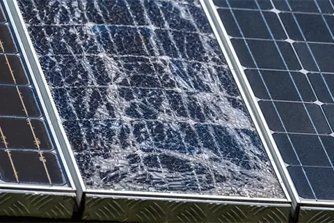 Close-up of solar panel with severely shattered glass across full module surface between undamaged panels