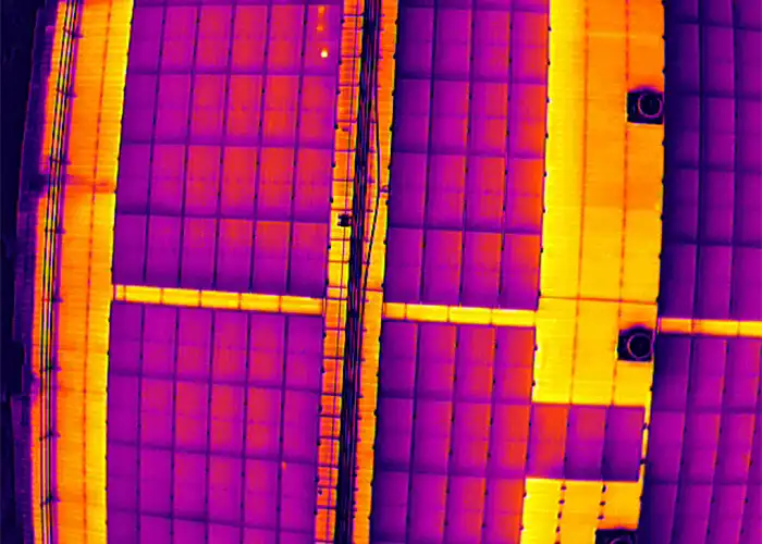 Aerial radiometric thermal image of rooftop solar panels showing purple-orange temperature variation across the array