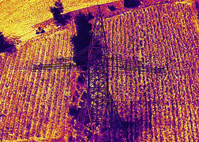 Aerial thermal image of transmission tower from above, tower in dark purple against orange-yellow agricultural field patterns
