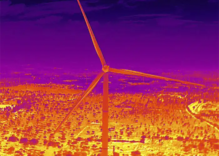 Thermal aerial image of wind turbine showing three blades and tower in orange against deep purple sky and warm landscape below