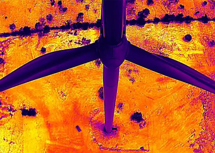 Overhead thermal image of wind turbine hub and three blades in star formation, blades cooler than surrounding ground