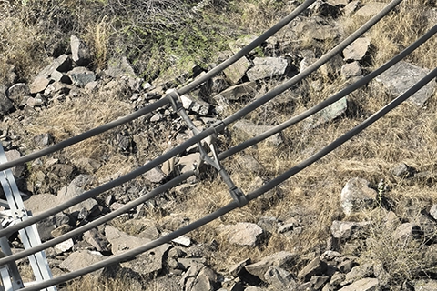 Bundle conductor spacer bridging parallel transmission cables over rocky terrain