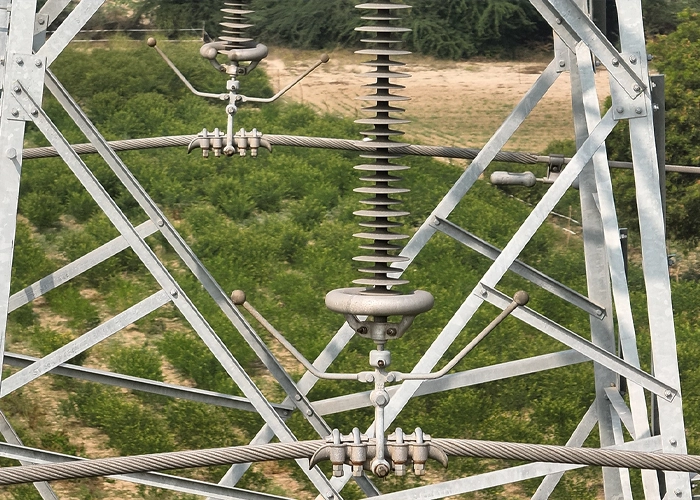 Close-up of insulator string, arcing horns, and strain clamp hardware on a transmission tower cross arm