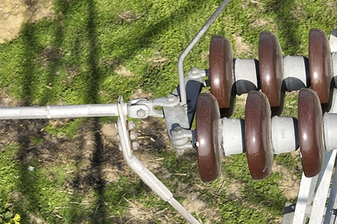 Strain insulator assembly with clamp hardware securing conductor at tension tower