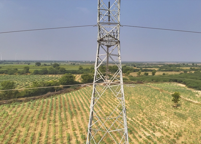 Aerial view of lattice transmission tower rising above farmland during drone inspection