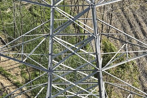 Aerial drone view looking down through the lattice cage of a transmission tower structure