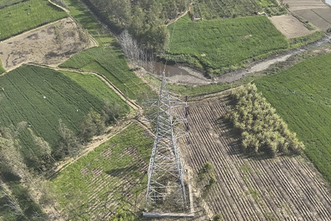 Bird's-eye drone view directly above a transmission tower base surrounded by farmland