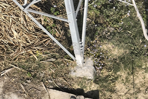 Transmission tower foundation leg set into concrete footing surrounded by vegetation