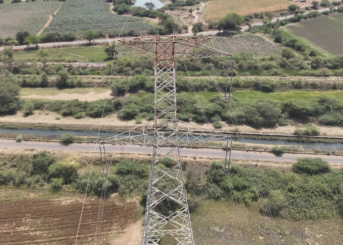 Aerial view of transmission tower with conductors spanning a road and canal crossing near farmland
