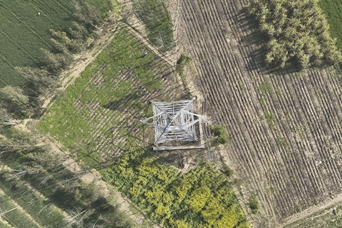 Bird's-eye drone view directly above a transmission tower base surrounded by farmland